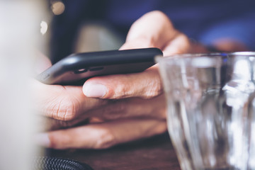 A man holding and using smart phone with glasses foreground in modern cafe