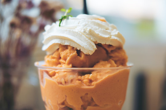 Close up image of Thai tea milk shake and whipped cream on the top in a glass with blue flower background 