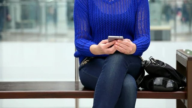 Young sad woman in casual clothes uses modern smartphone while waiting somebody in big modern mall interior. Than puts cell phone into black bag. Real time full hd video footage.