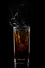 A glass of whiskey and ice cube on a black background