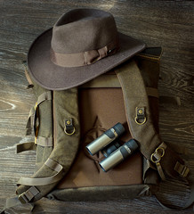 Hat, Binoculars, backpack lie together for travel on wood floor