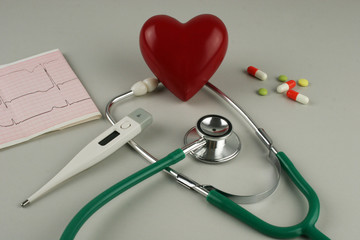 Stethoscope, electrocardiogram, thermometer, and a red heart on a gray background.