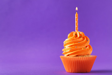 Tasty cupcakes with candle on a purple background