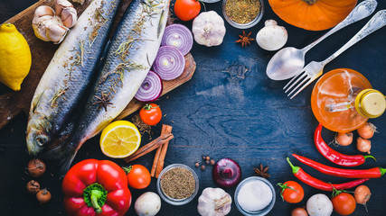 Fresh fish with vegetables, spices and oil. On a black wooden background. Free space for text . Top view