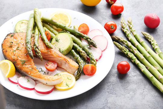 Steak of salmon with asparagus and vegetables on grey wooden table