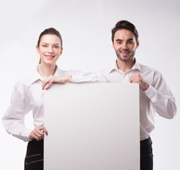 Young happy couple showing presentation pointing on placard over gray background