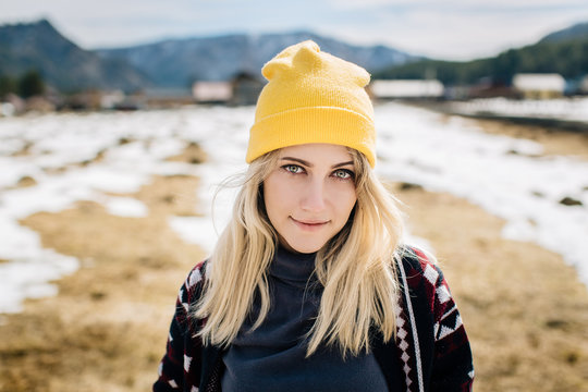portrait of a girl with blond hair in a knitted yellow hat in a rural mountain area