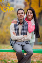 photo of cute couple sitting on the bench on the wonderful autumn trees background