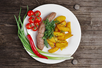 Top view of homemade sausage with fried potato, tomato cherry, pepper and green onion on wooden table.