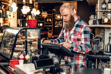 A man at the counter using cash register in a coffee shop.