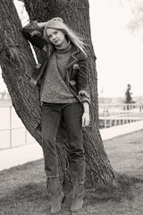 Fototapeta na wymiar A slim young woman in jeans with a leather American jacket and brown boots for a walk in a beautiful day outdoors near the beach and trees and outdoors in a good mood