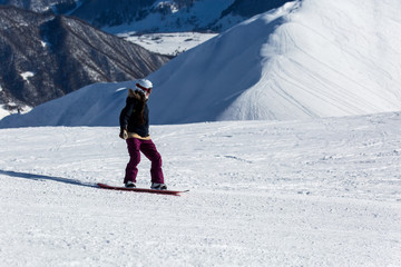 women snowboarder snowboarding on fresh white snow with ski slope on Sunny winter day