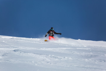 Naklejka na ściany i meble snowboarder snowboarding on fresh white snow with ski slope on Sunny winter day