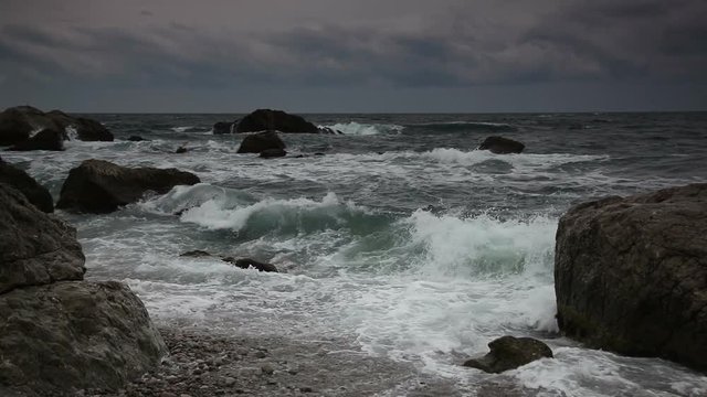 Sea waves break about coastal stones during inflow at sunset