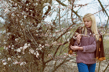 Young beautiful cute blonde girl in a botanical wild garden with flowering spring trees dreamy tender attractive with attractive appearance