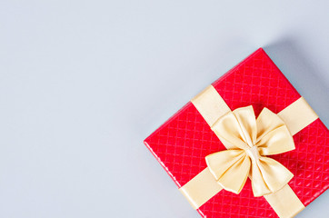 Red gift box with gold ribbon on gray background.
