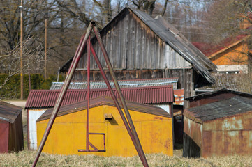 Old metal swings on bright yellow wall background on a sunny day with old buildings in the distance. Street photography, no people.