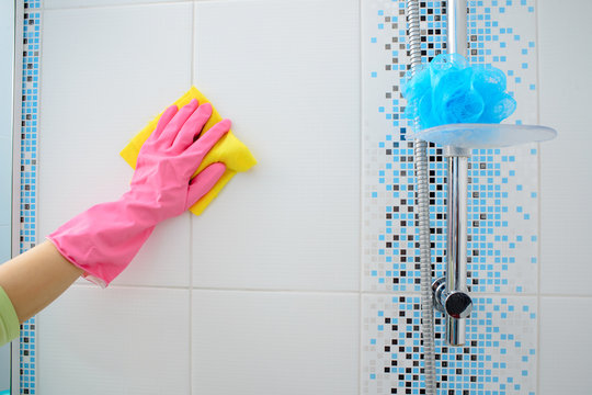 A woman washer is cleaning tiled surface in kitchen. The girl in pink gloves - Powered by Adobe