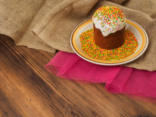 Easter cake, ceramic bowl with colorful sweet powder. Russian and Ukrainian, orthodox slavic traditional Easter kulich on rural background from old wood, red mesh paper and burlap.