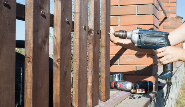 Woman hands drilling wood plank fence to metal construction. Building a wooden fence with a drill and screw.