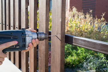 Woman hands drilling wood plank fence to metal construction. Building a wooden fence with a drill...
