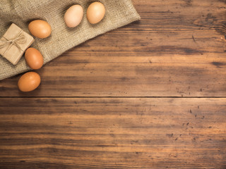 Brown chicken eggs and gift box lay on a piece of burlap on a wooden table from the old boards. Top view. Fresh chicken eggs close-up, background for advertising or Easter greetings, rustic style