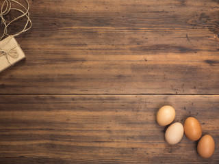Easter eggs, gift box on old wooden table from planks. Top view with space for your design, Easter greetings or advertising. Rustic background. Composition of eggs and gift boxes tied with string