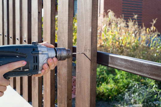 Woman hands drilling wood plank fence to metal construction. Building a wooden fence with a drill and screw.