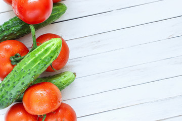 Fresh cucumbers and tomatoes on a white wooden background. Place for text.