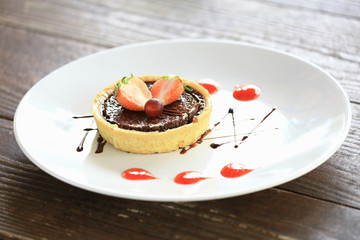 Delicious chocolate tart with strawberry and grape on white plate, closeup