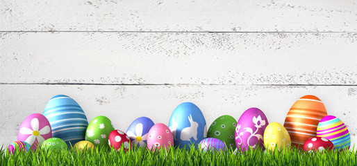 Fototapeta premium Bunte Ostereier im Gras vor weißer Holzwand