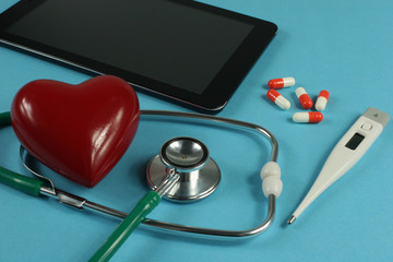 Stethoscope, tablet computer,thermometer and heart on blue background.