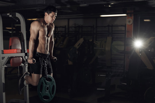 Muscular bodybuilder working out in gym doing exercises on parallel bars. Athlitic male naked torso.