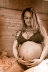 pregnant young woman in tailor's seat holds her belly and looks happy at it in dessus Schwangere Frau mit Babybauch in Desous	 Schwangere Frau mit Babybauch in Desous