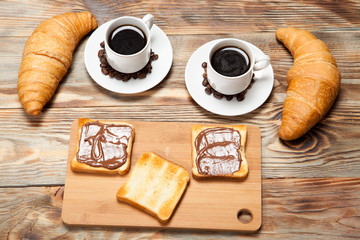 Two cups of coffee, croissant, toast and chocolate on wooden table