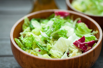 A dish of fresh salad frisse, Romano and radiccio with olive oil, salt and freshly ground percec in a wooden bowl