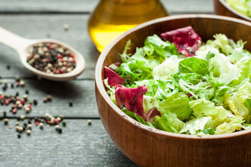 A dish of fresh salad frisse, Romano and radiccio with olive oil, salt and freshly ground percec in a wooden bowl