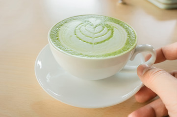 a man's hand holding a hot matcha green tea cup