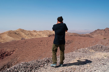 Fototapeta premium Medio Oriente, 10/03/2013: un uomo di spalle fotografa il paesaggio deserto sulla strada che collega la Riserva Biosfera di Dana, la più grande riserva naturale della Giordania, a Petra