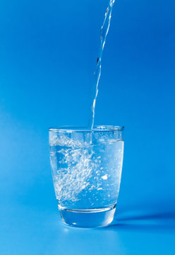Pouring water into glass on blue background
