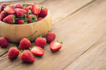 Fresh strawberries in a bowl on wooden background.