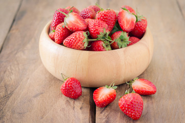 Fresh strawberries in a bowl on wooden background.