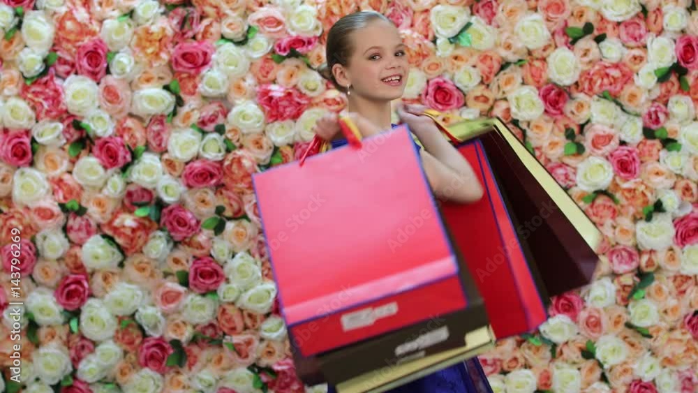 Poster Childrens shopping. Portrait of smiling little girl in blue dress, background of bright floral wall