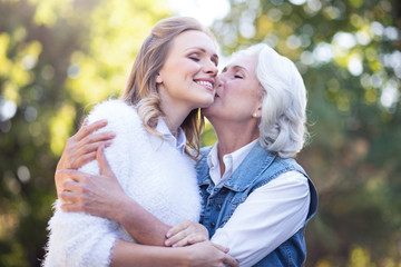 Aged mother kissing mature daughter in the park
