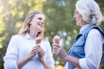 Aged woman eating ice cream with mature daughter outdoors