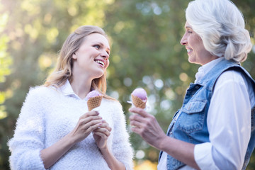 Fototapeta premium Aged woman eating ice cream with mature daughter outdoors