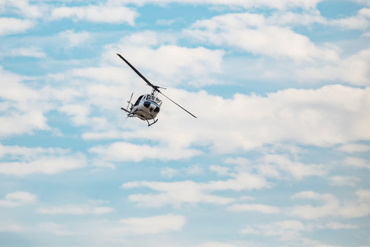 White helicopter flying in the blue sky with clouds