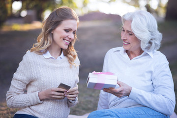 Caring aged mother giving present to mature daughter in the park