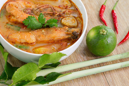 Tom yum kung in white bowl and ingredients on wooden table