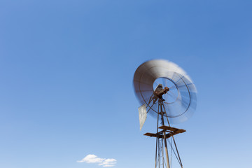 Close up wide angle image of a windmill / windpomp with spinning blades, pumping water in the Tankwa Karoo in South Africa on a hot summersday